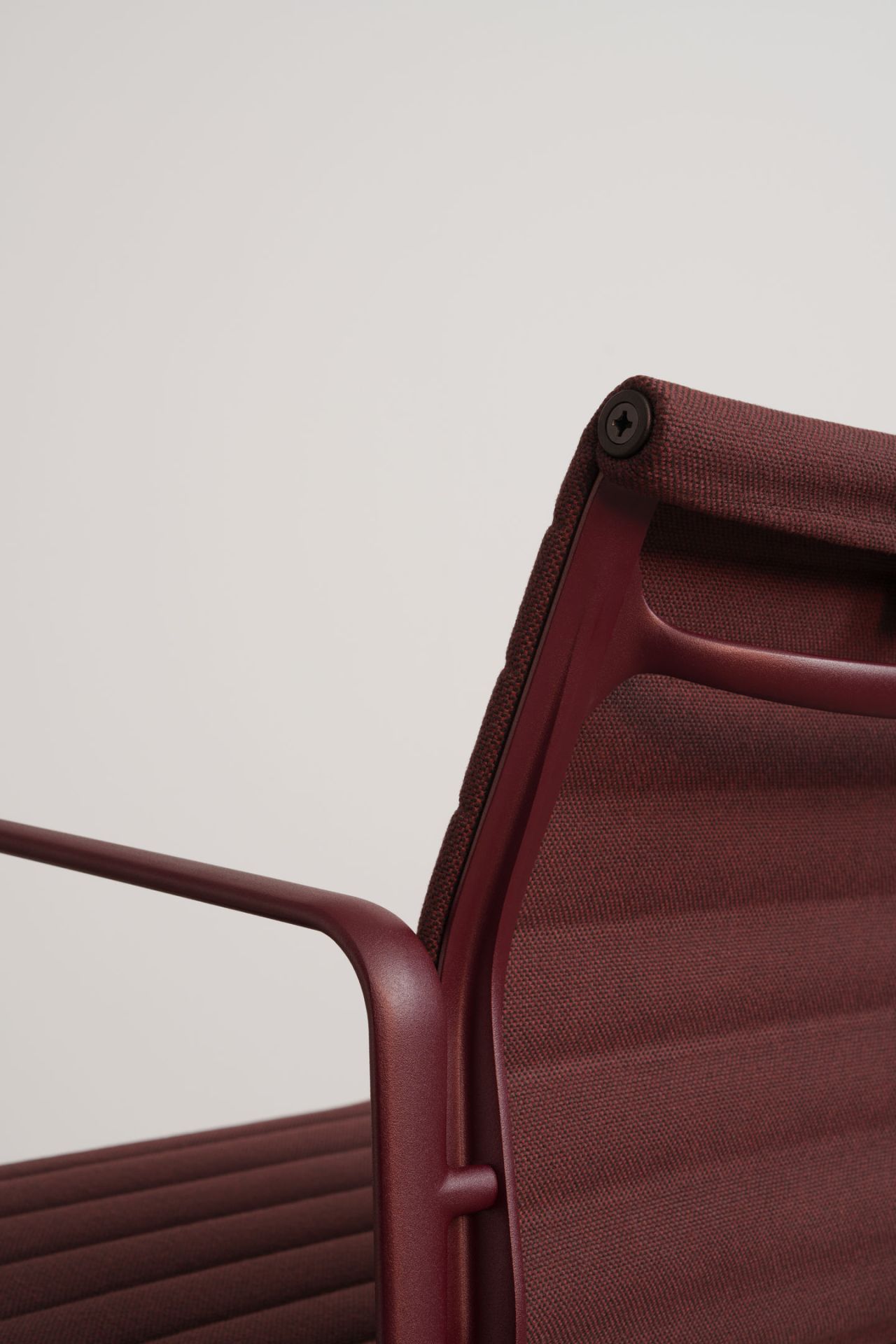 Detailaufnahme des Aluminium Chair EA 108 von Vitra in Burgunderrot, Fokus auf Armlehne und Rückenlehne.