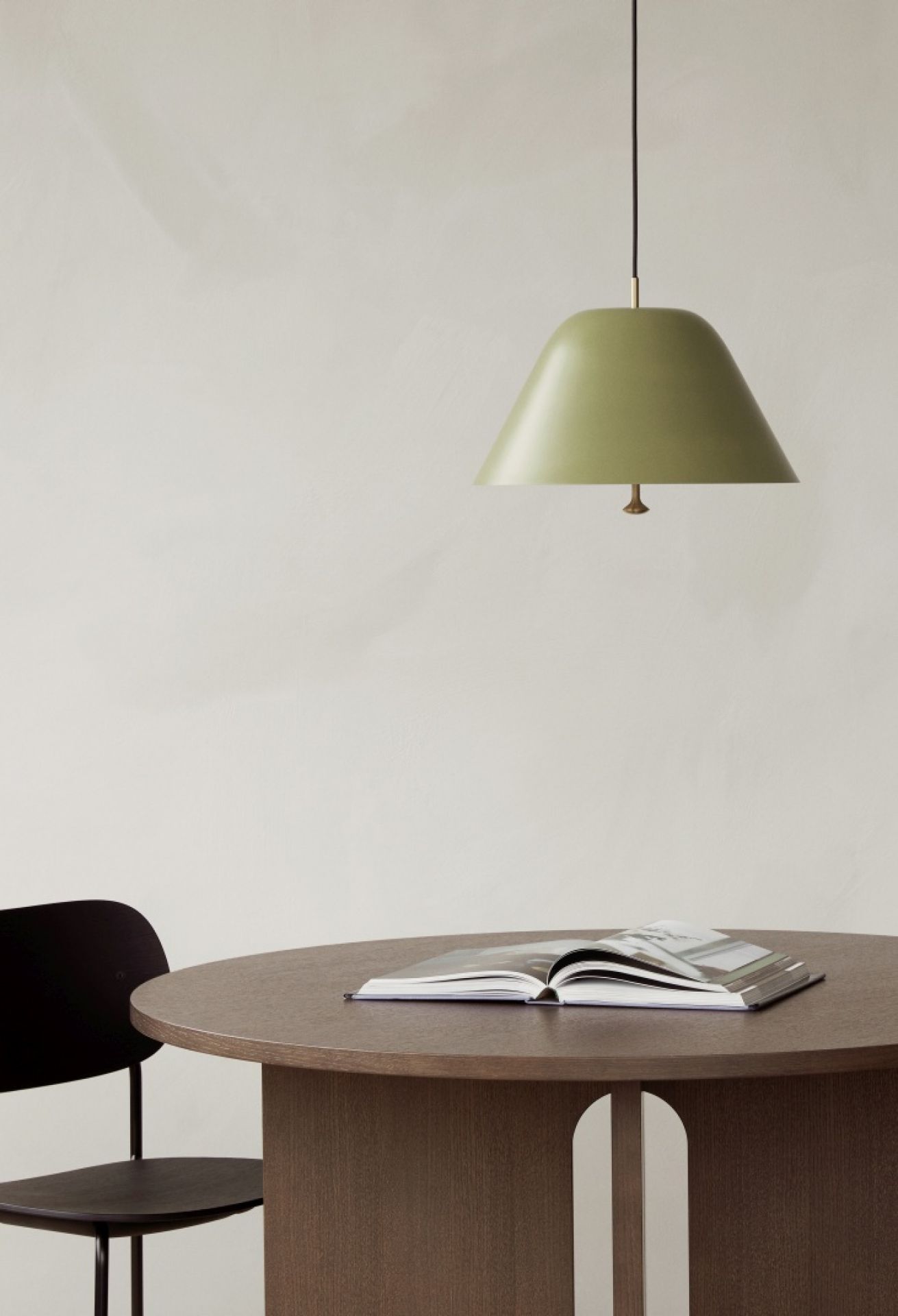 Androgyne Esstisch aus dunkler Eiche mit Sandstein-Optik. Runder Holztisch mit Buch und Lampe.