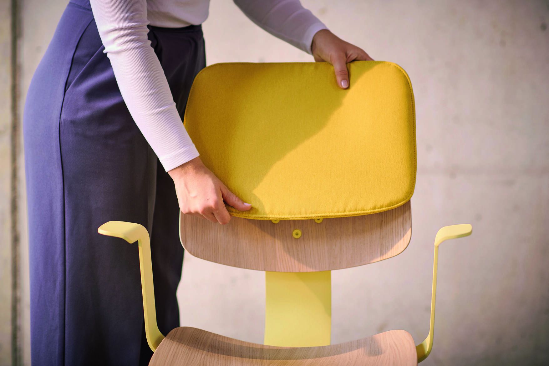 Frau befestigt gelbes Sitzkissen auf Wilkhahn 228 WiChair Bürostuhl, ergonomischer Drehstuhl mit Armlehnen für Büro und Homeoffice.