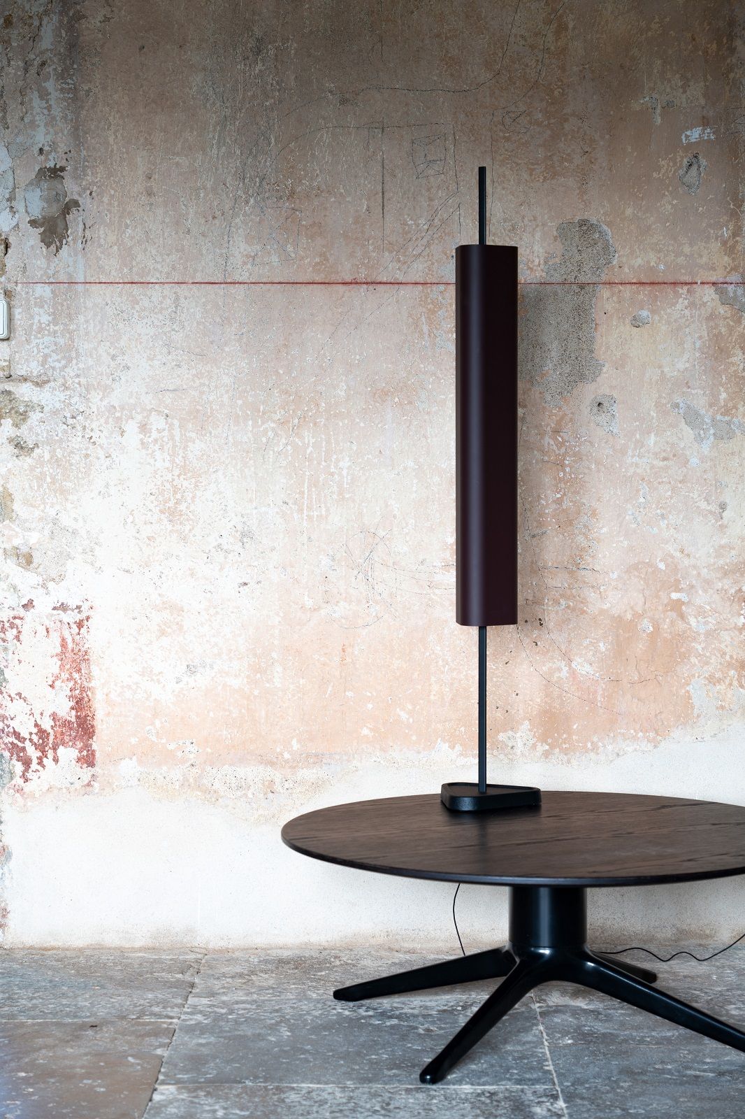 Emi Table Tischleuchte von Flos in Deep Rot auf einem schwarzen Tisch vor Wand.