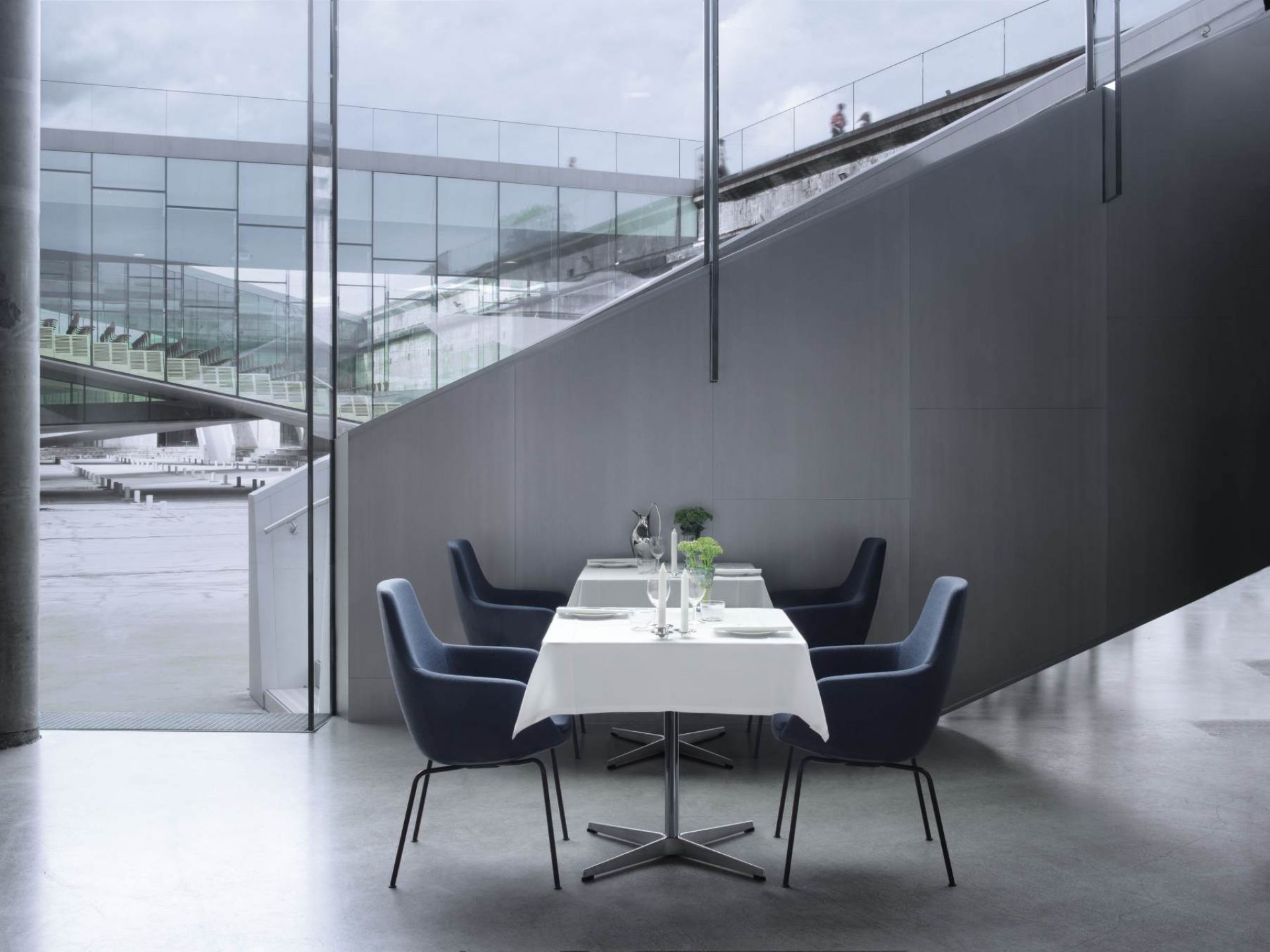 Fritz Hansen Little Giraffe Stuhl mit blauem Bezug an gedecktem Tisch in modernem Ambiente.