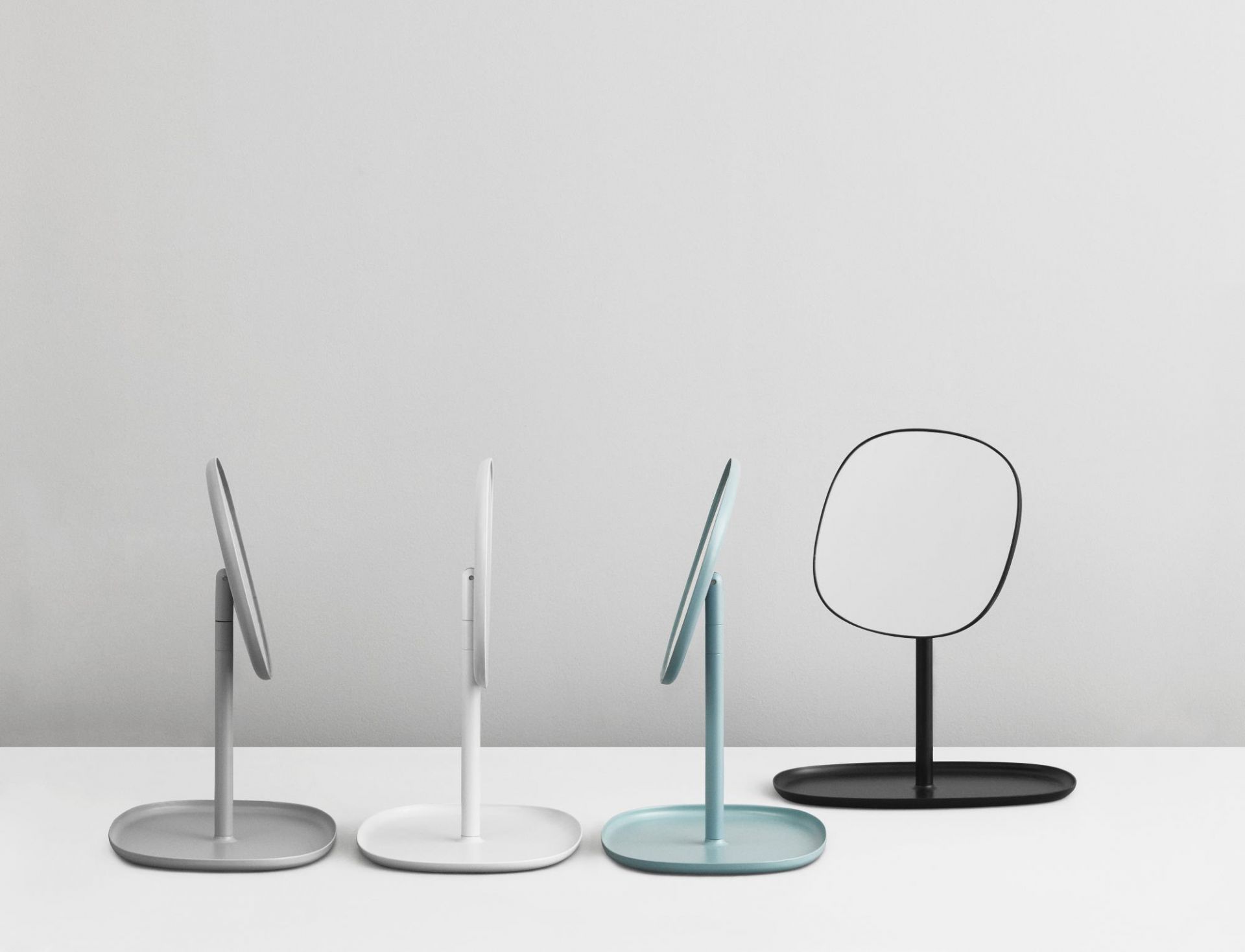 Verschiedenfarbige Normann Copenhagen Flip Spiegel: Grau, Weiß, Blau und Schwarz auf einem weißen Tisch.