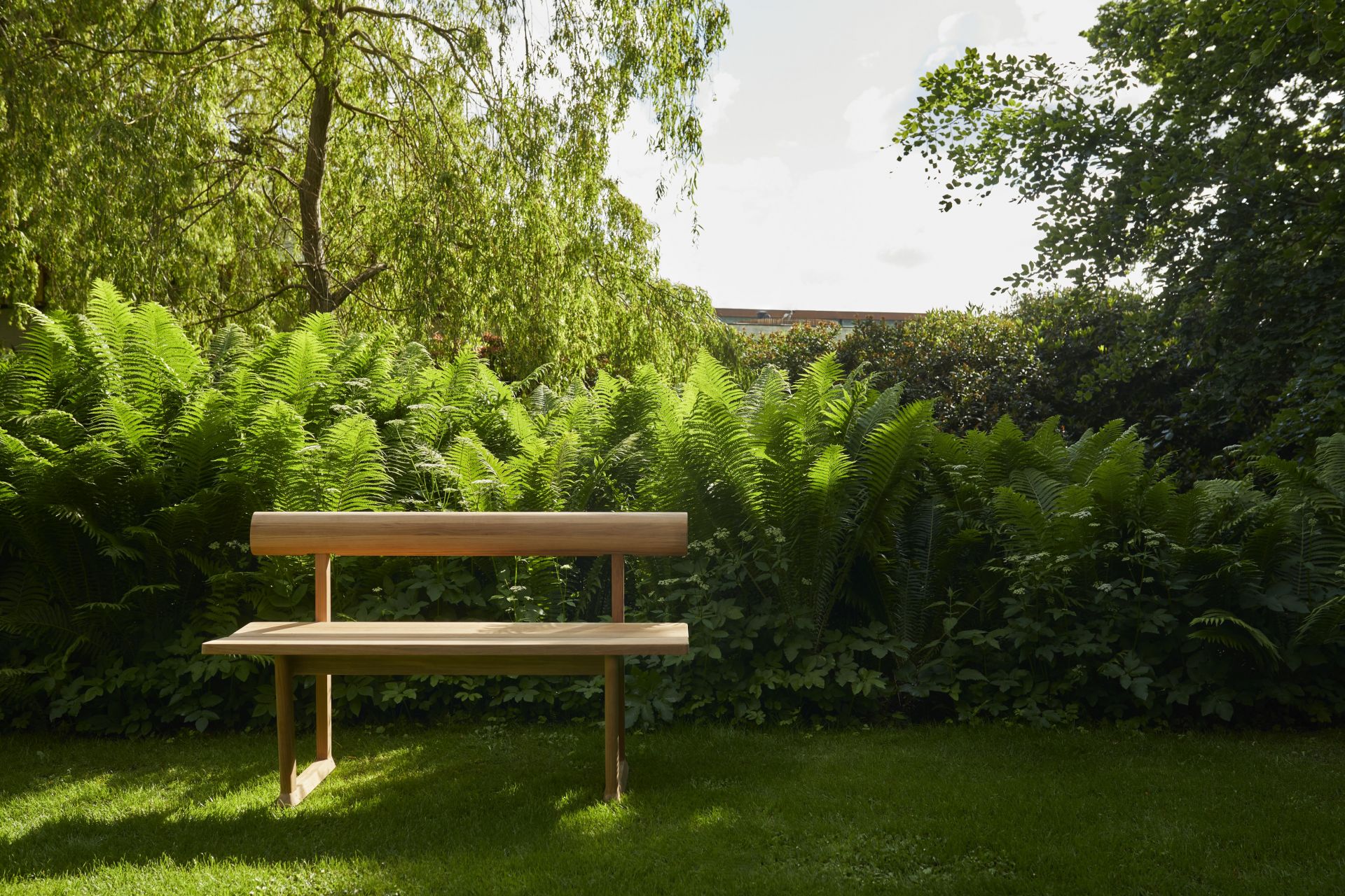Banco Bank aus Teakholz von Skagerak by Fritz Hansen im Garten, umgeben von Grünpflanzen.