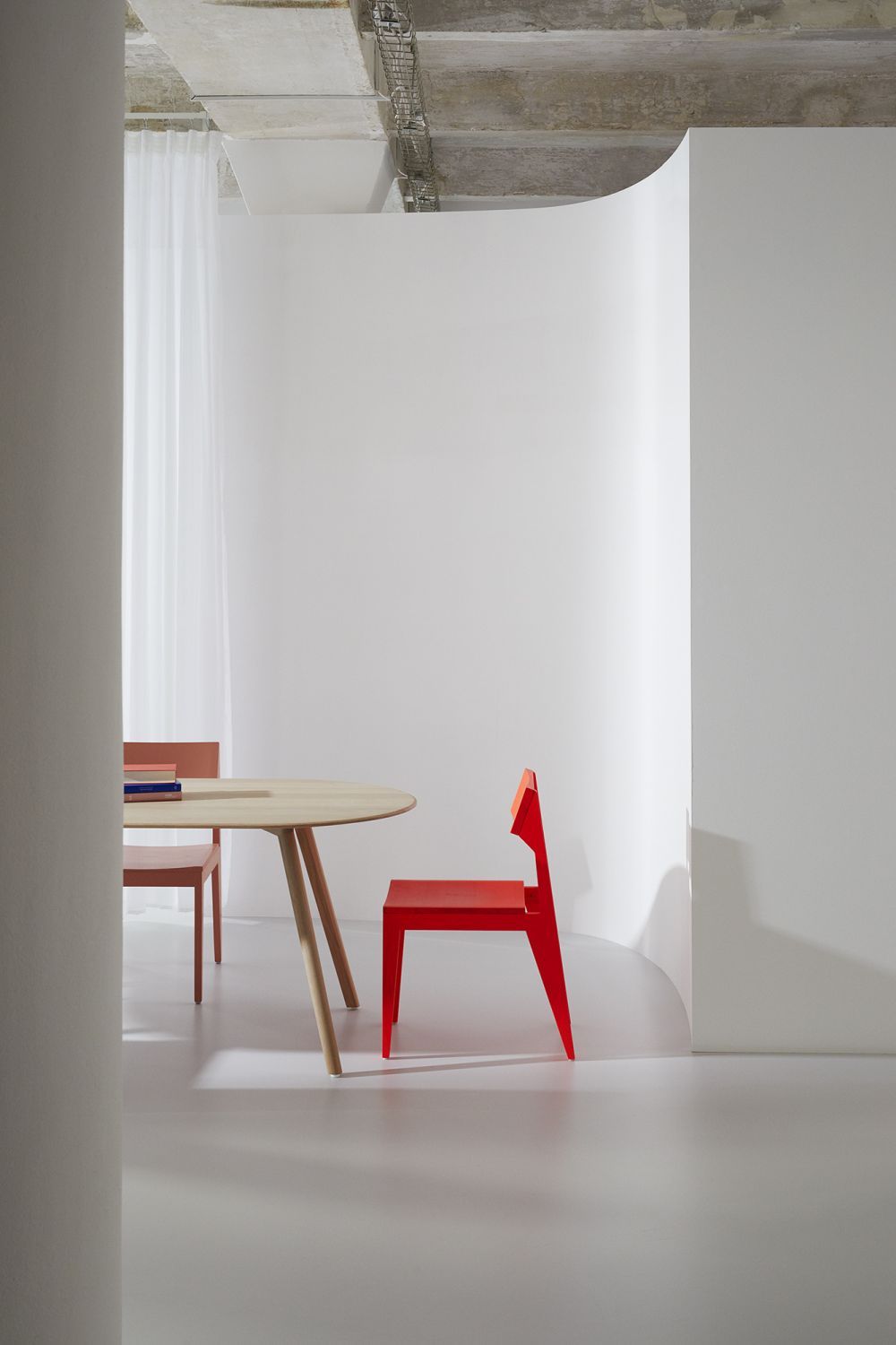Roter Schulz Stuhl OUT neben Holztisch in minimalistischem, hellem Raum. Design Stühle und Möbel.