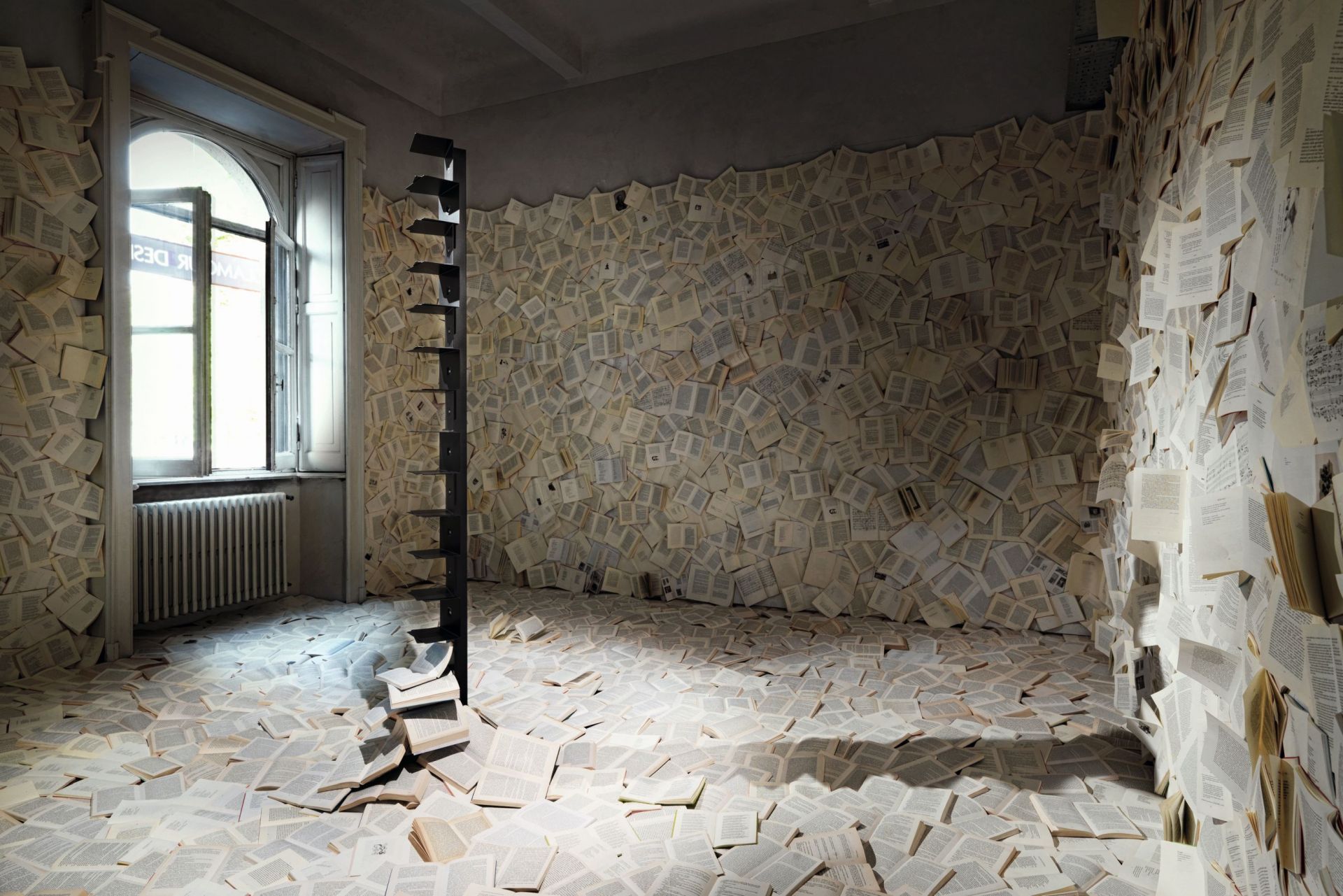 Ptolomeo Bücherregal in einem Raum, dessen Wände und Boden mit offenen Büchern bedeckt sind.