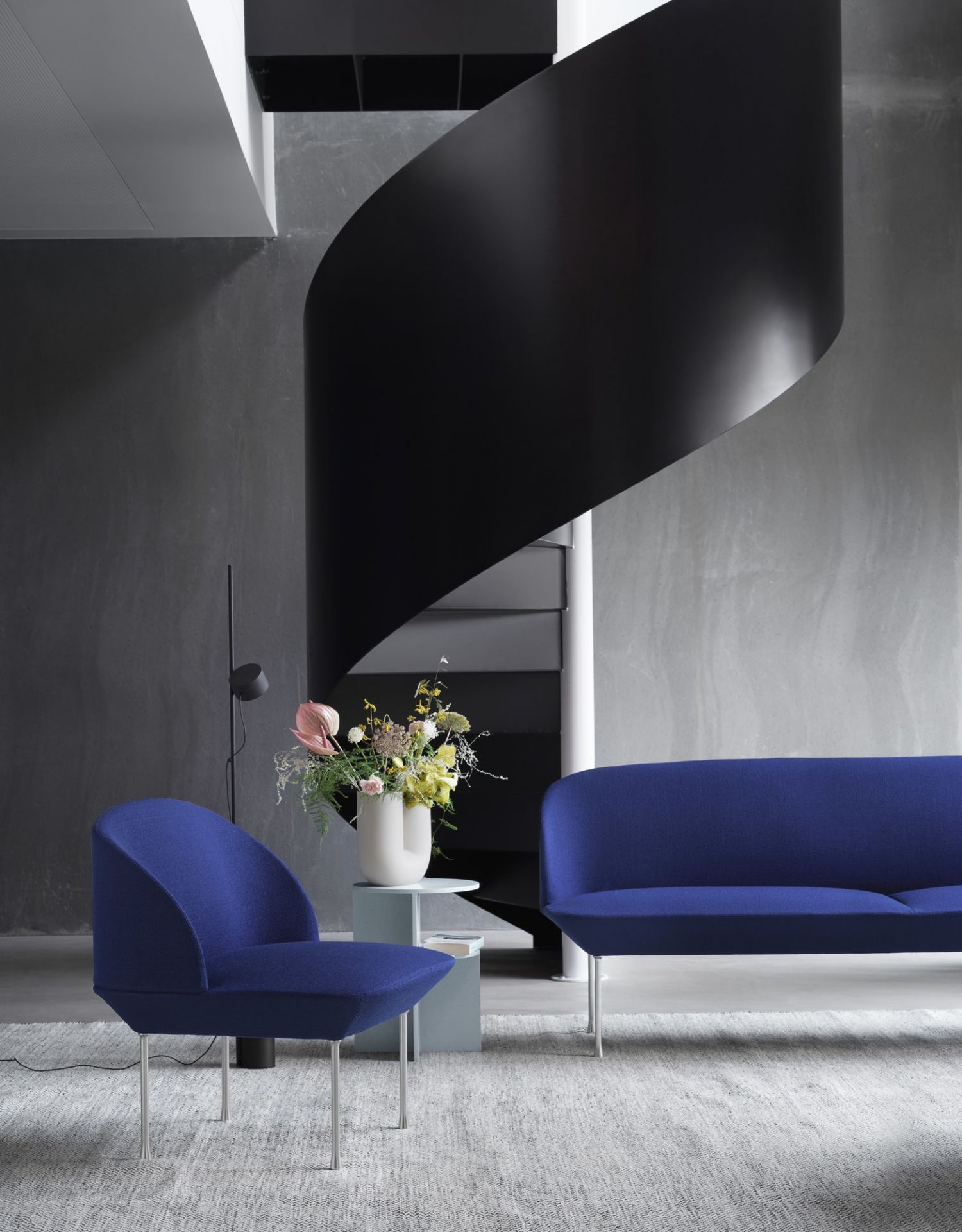 Blaues Oslo Sofa und Sessel von Muuto in modernem Wohnzimmer mit Wendeltreppe.