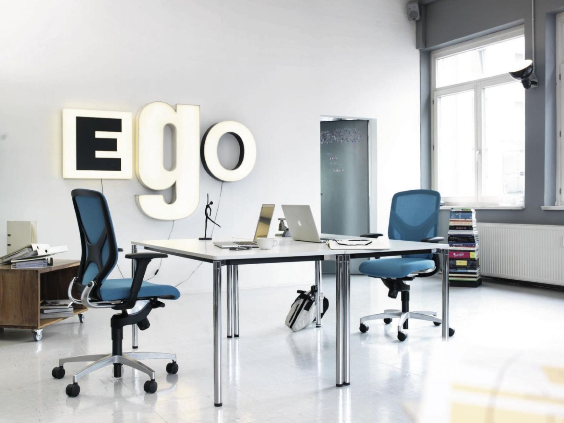 Modernes Büro mit weißen Schreibtischen, blauen Bürostühlen, Laptops und minimalistischer Dekoration für stilvolles Arbeiten.
