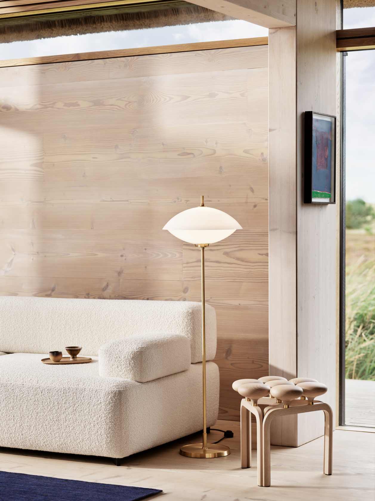 Heller Wohnraum mit Fritz Hansen Utzon Hocker aus Holz, Stehlampe und Sofa.