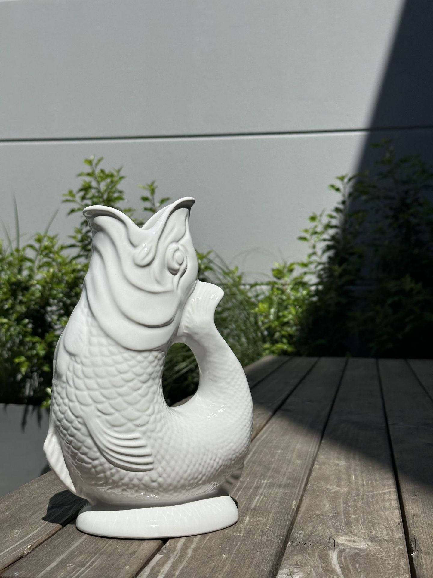 Weiße Gluckigluck Fischkaraffe XL auf Holzterrasse. Dekorative Wasserkaraffe und Vase in Fischform.