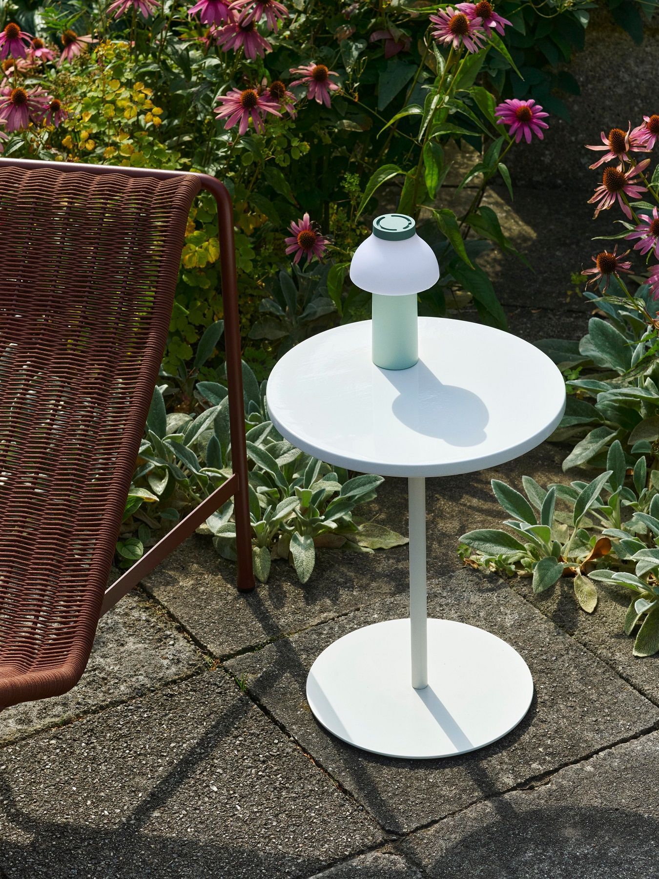 Nahaufnahme des weißen Hay Pyro Coffee Table Outdoor Couchtischs im Garten neben einem braunen Stuhl.