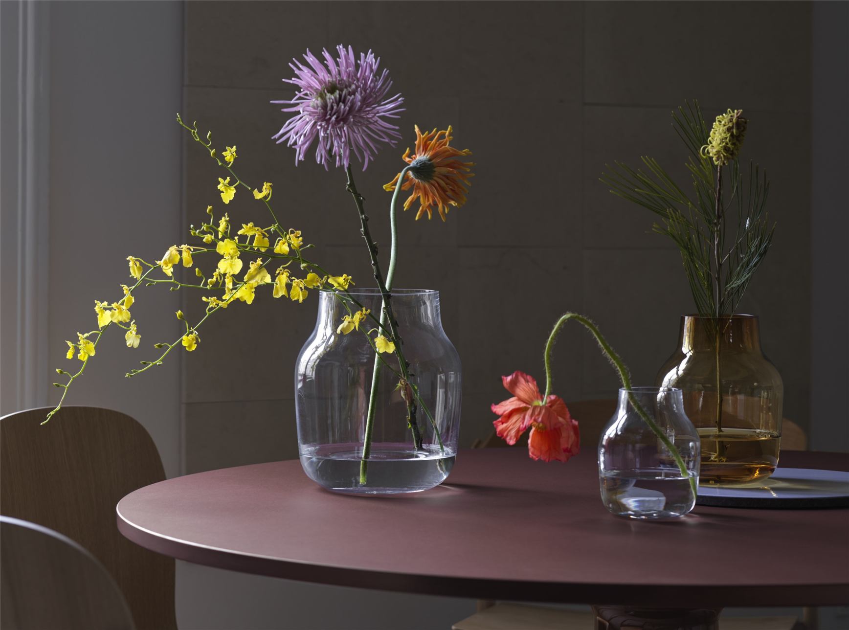 MIDST Table Esstisch von Muuto, runde Tischplatte in Bordeauxrot mit Blumenvasen als Dekoration.