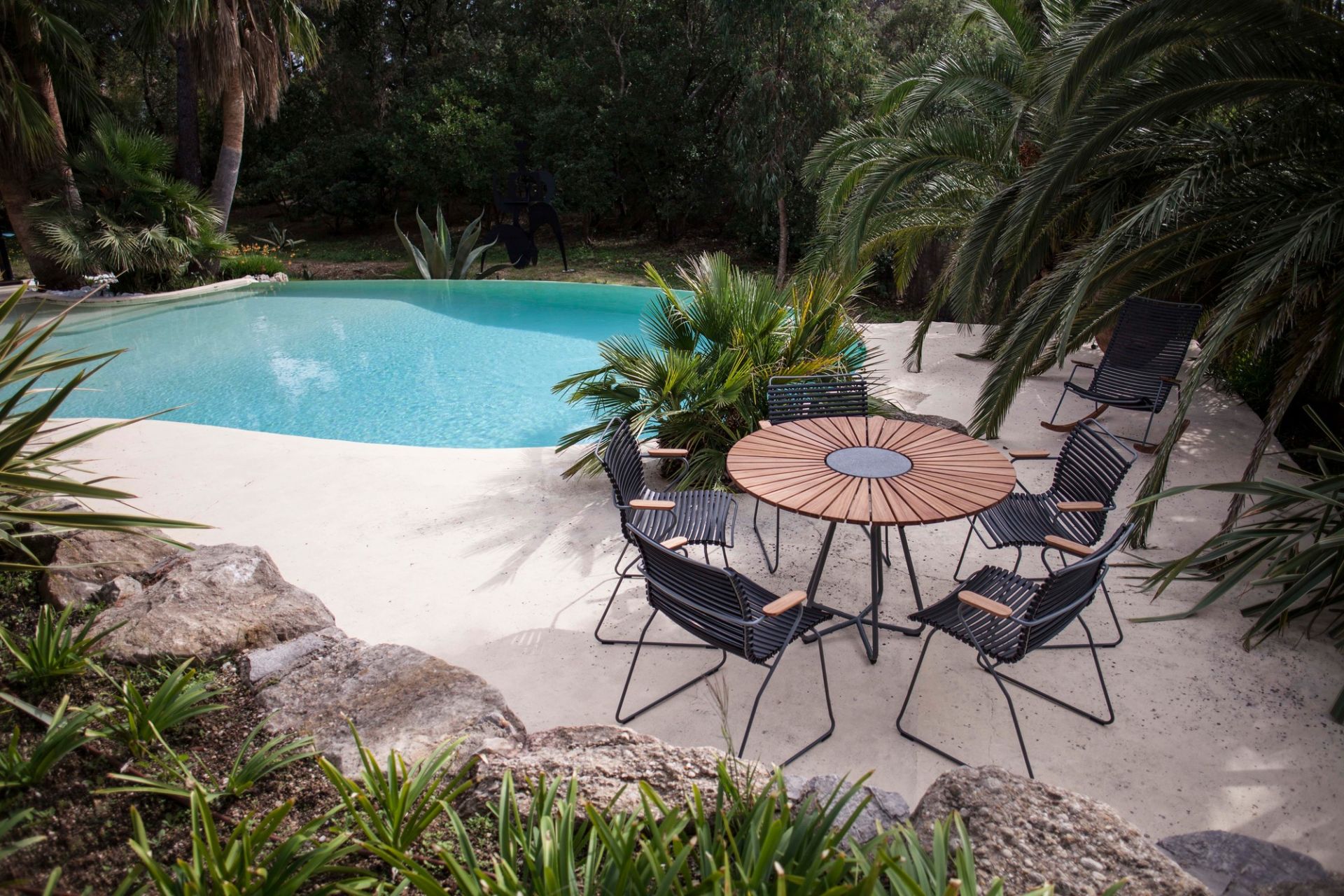 Houe Circle Outdoor Tisch 150 cm mit Stühlen neben Pool in tropischer Gartenanlage.