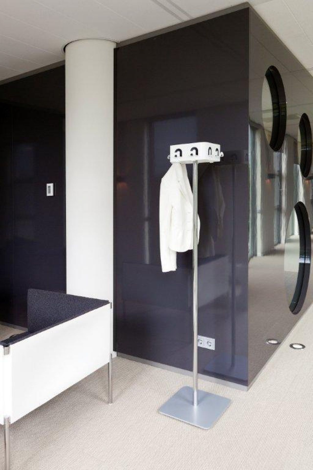 Freistehende Garderobe aus Metall mit weißem Blazer in modernem Büro- oder Empfangsbereich.