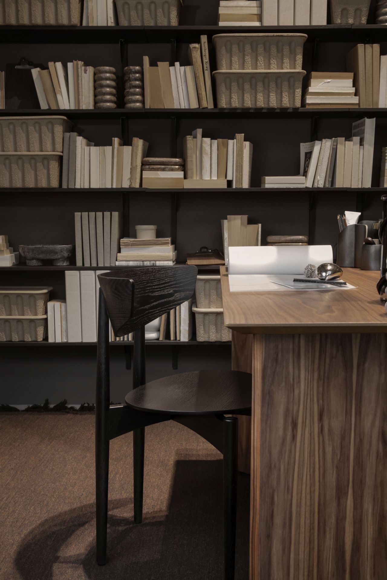 Schwarzer Herman Esszimmerstuhl von Ferm Living mit Holzgestell vor Bücherregal und Schreibtisch.