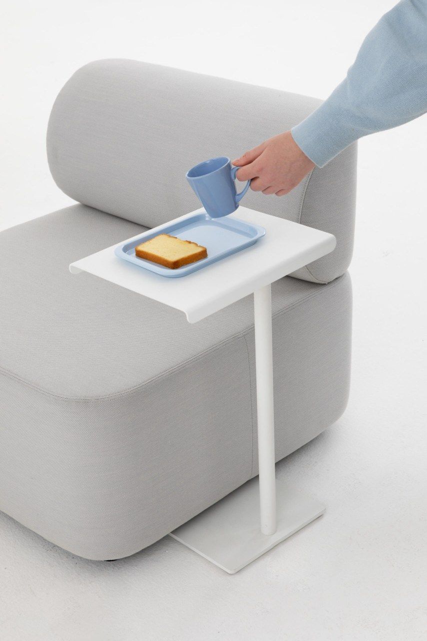Mezza Sitzelement mit Rücken von Cascando, graues modulares Sofa mit Beistelltisch und Person mit Tasse.