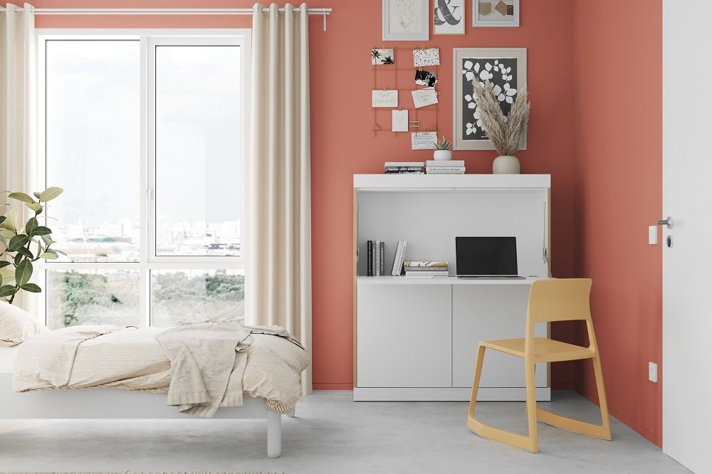 FLAI Home-Office Sekretär von Müller Möbelwerkstätten in Weiß mit gelbem Stuhl und Bett im Hintergrund.