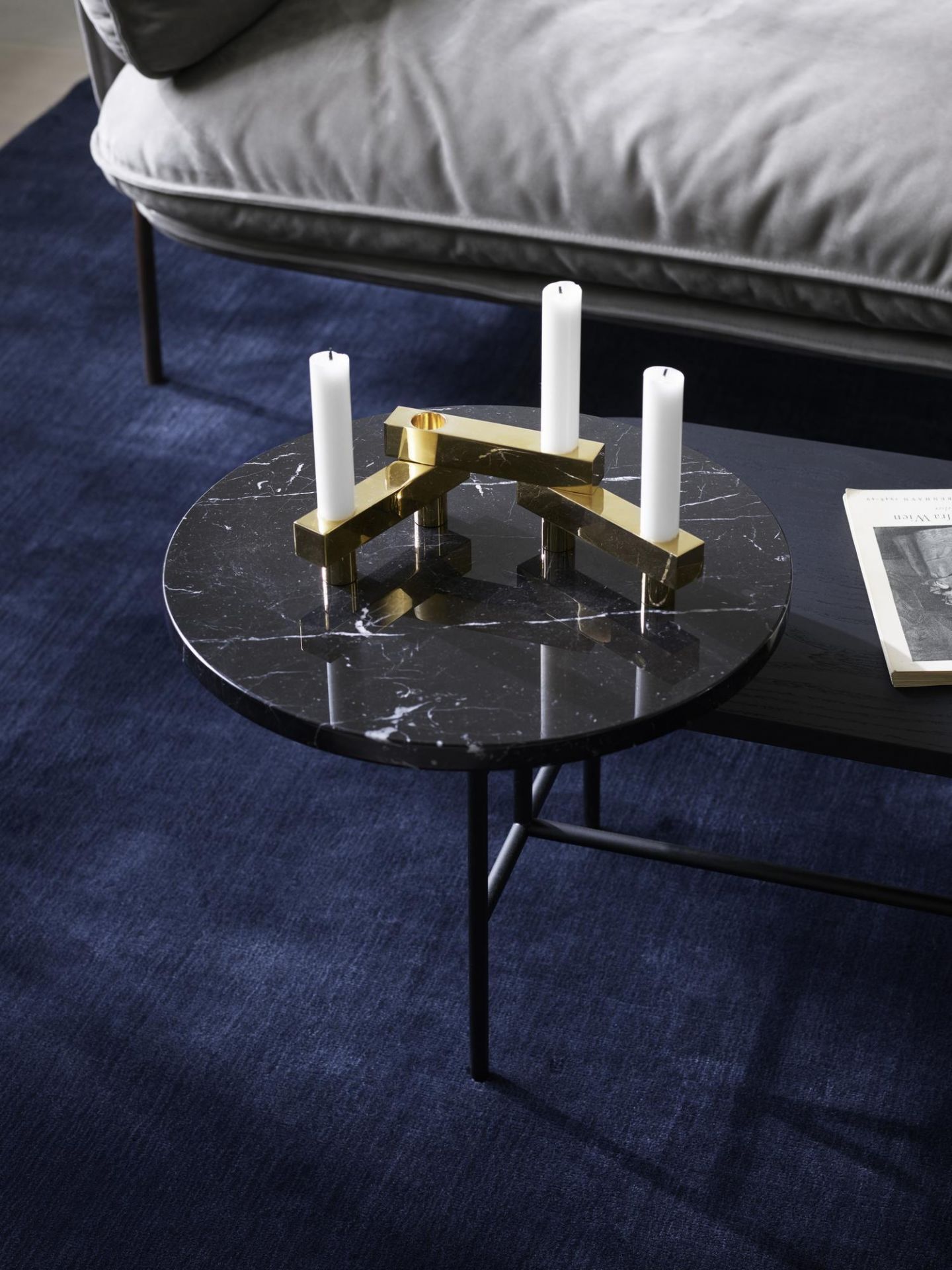 AndTradition Palette Table JH7 Couchtisch mit Marmorplatte, Kerzen und goldenem Kerzenständer auf blauem Teppich.