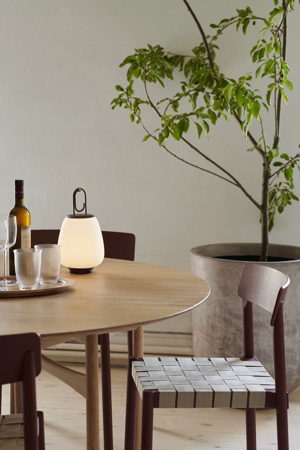 AndTradition Betty TK1 Stuhl mit gewebter Sitzfläche an Holztisch mit Lampe und Dekoration.