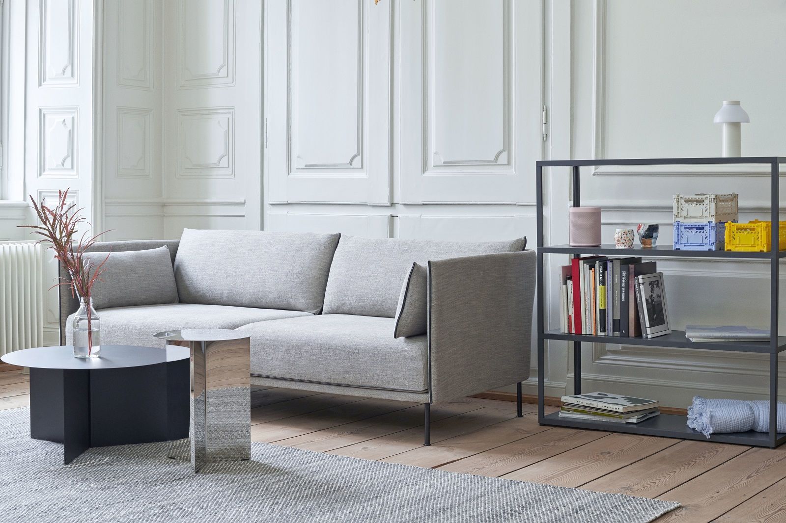 Helles Wohnzimmer mit grauem Silhouette Sofa 2-Sitzer Low Hay, Couchtischen und Bücherregal auf Holzboden.