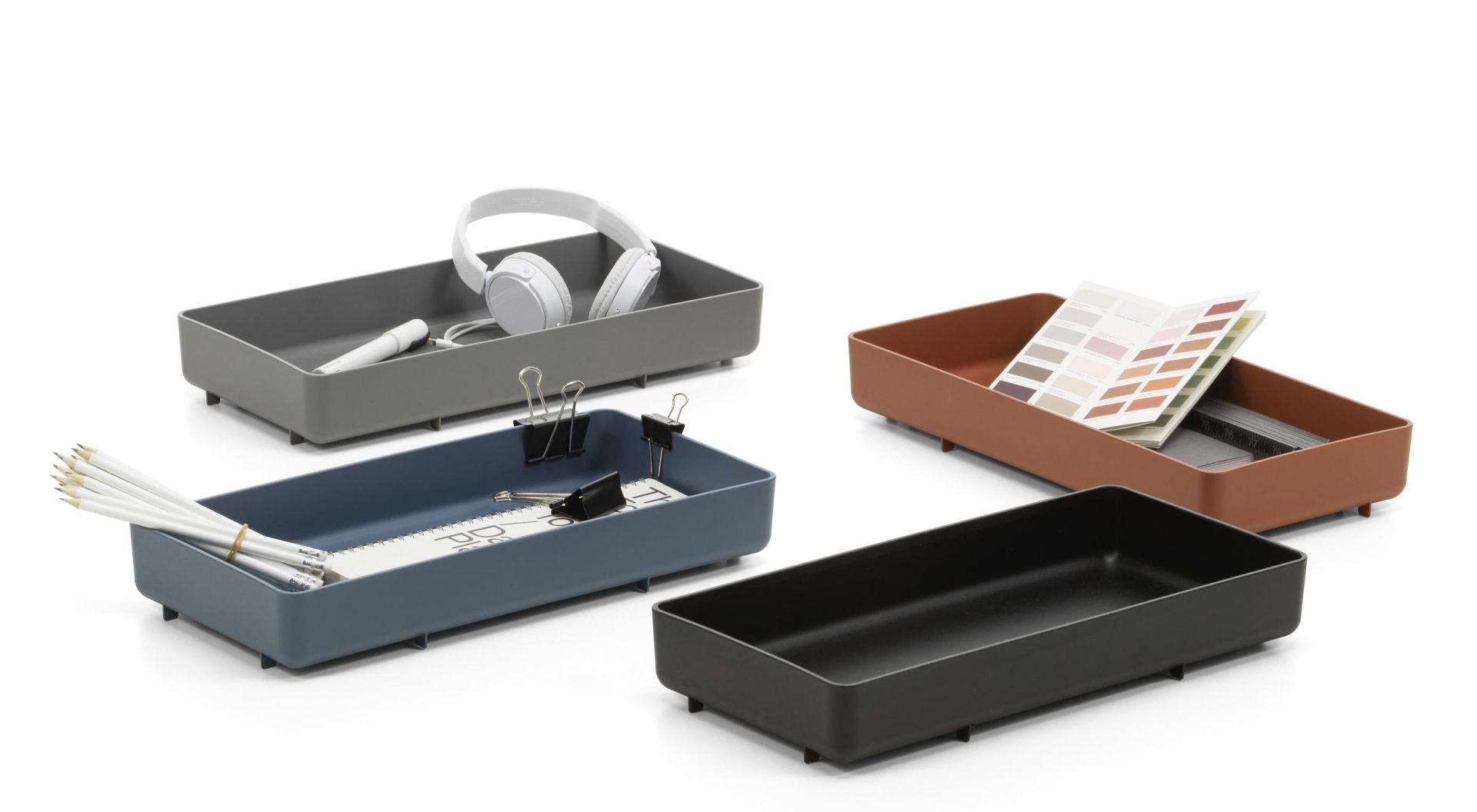 Vier farbige Vitra Chap Tray RE Tabletts zur Aufbewahrung von Büroartikeln auf weißem Hintergrund.
