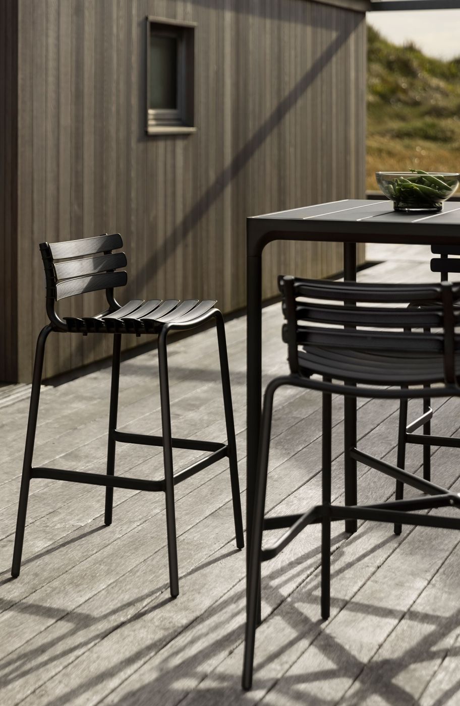 Nahaufnahme von Houe Four Bar Tisch und Barstühlen für den Außenbereich auf einer Holzterrasse.