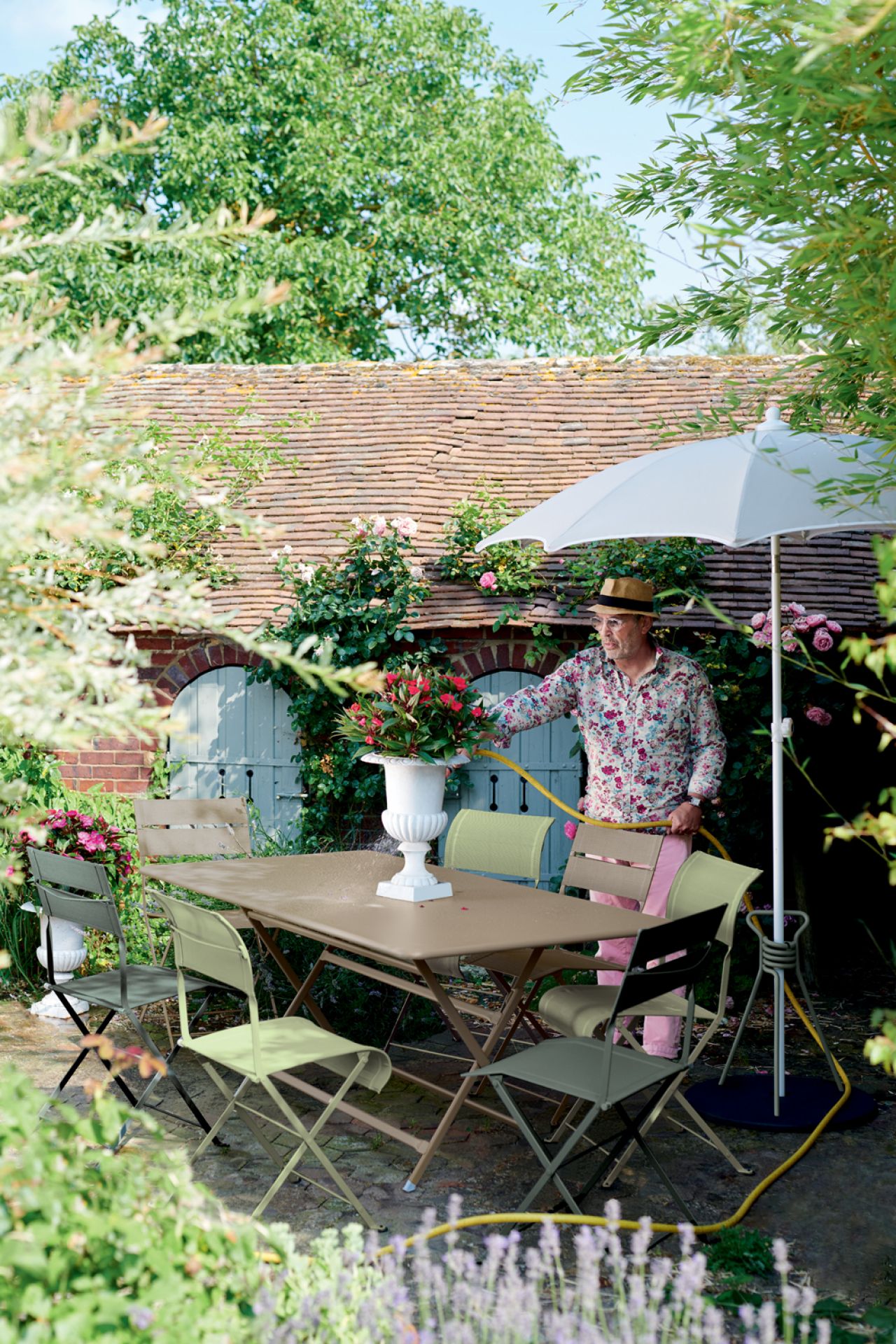 Caractere Klapptisch von Fermob im Garten mit Person, Sonnenschirm und Stühlen für entspannte Stunden im Freien.