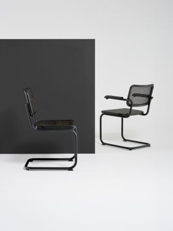 Zwei schwarze Thonet S 64 V Freischwinger Stühle mit Stahlrohrgestell und Wiener Geflecht vor monochromem Hintergrund.
