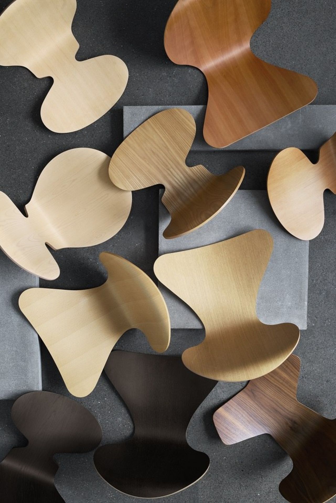Mehrere Fritz Hansen Series 7 Junior Chair Kinderstühle in verschiedenen Holzfarben auf grauem Hintergrund.