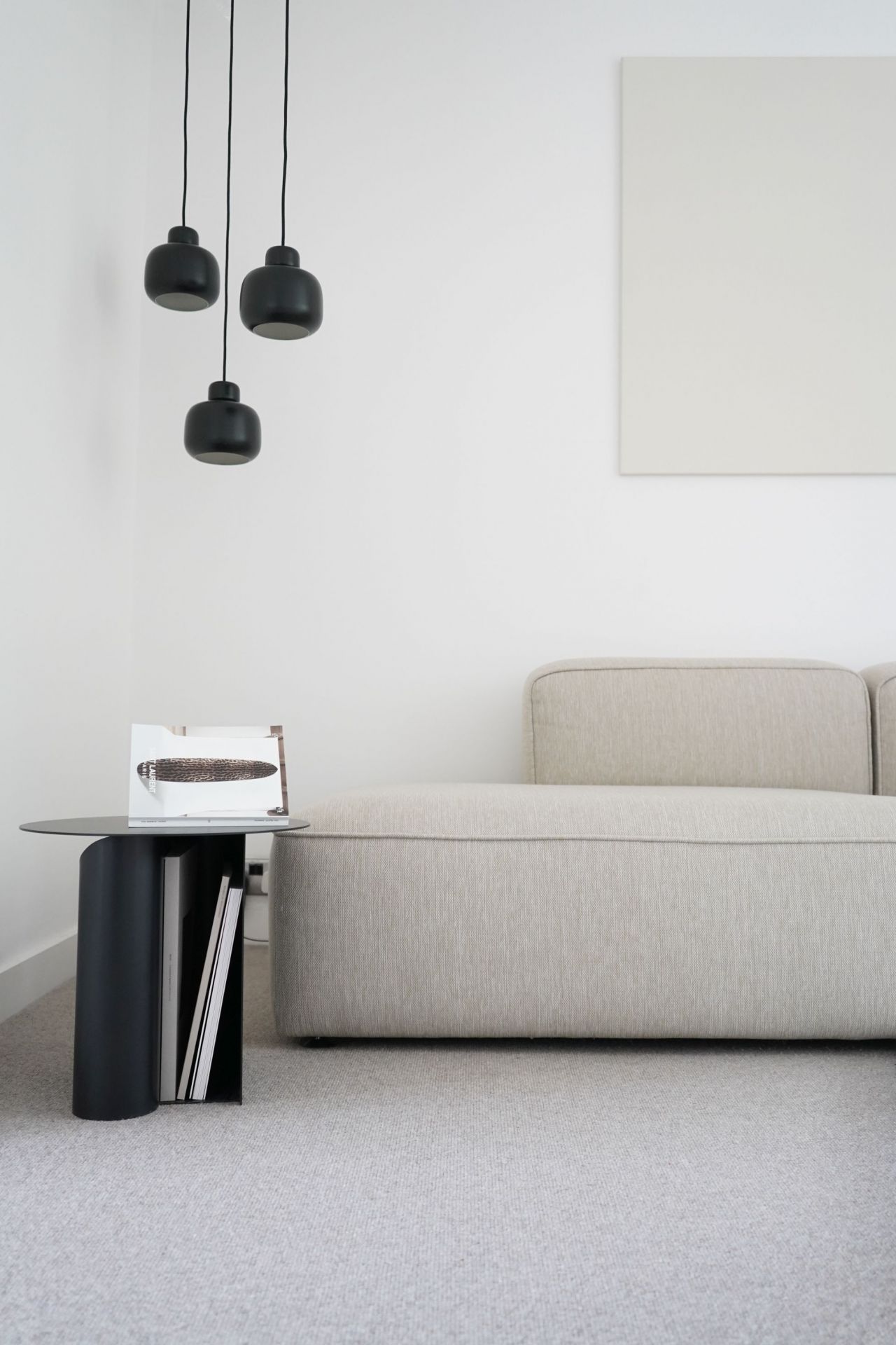 Nahaufnahme von drei schwarzen Stone Pendant Pendelleuchten von Woud über einem minimalistischen Wohnzimmer mit Sofa.
