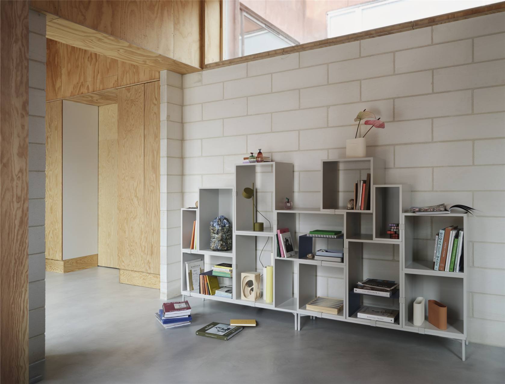 Muuto Post Table Lamp Tischleuchte in Braun-Grün auf einem Regal mit Büchern.