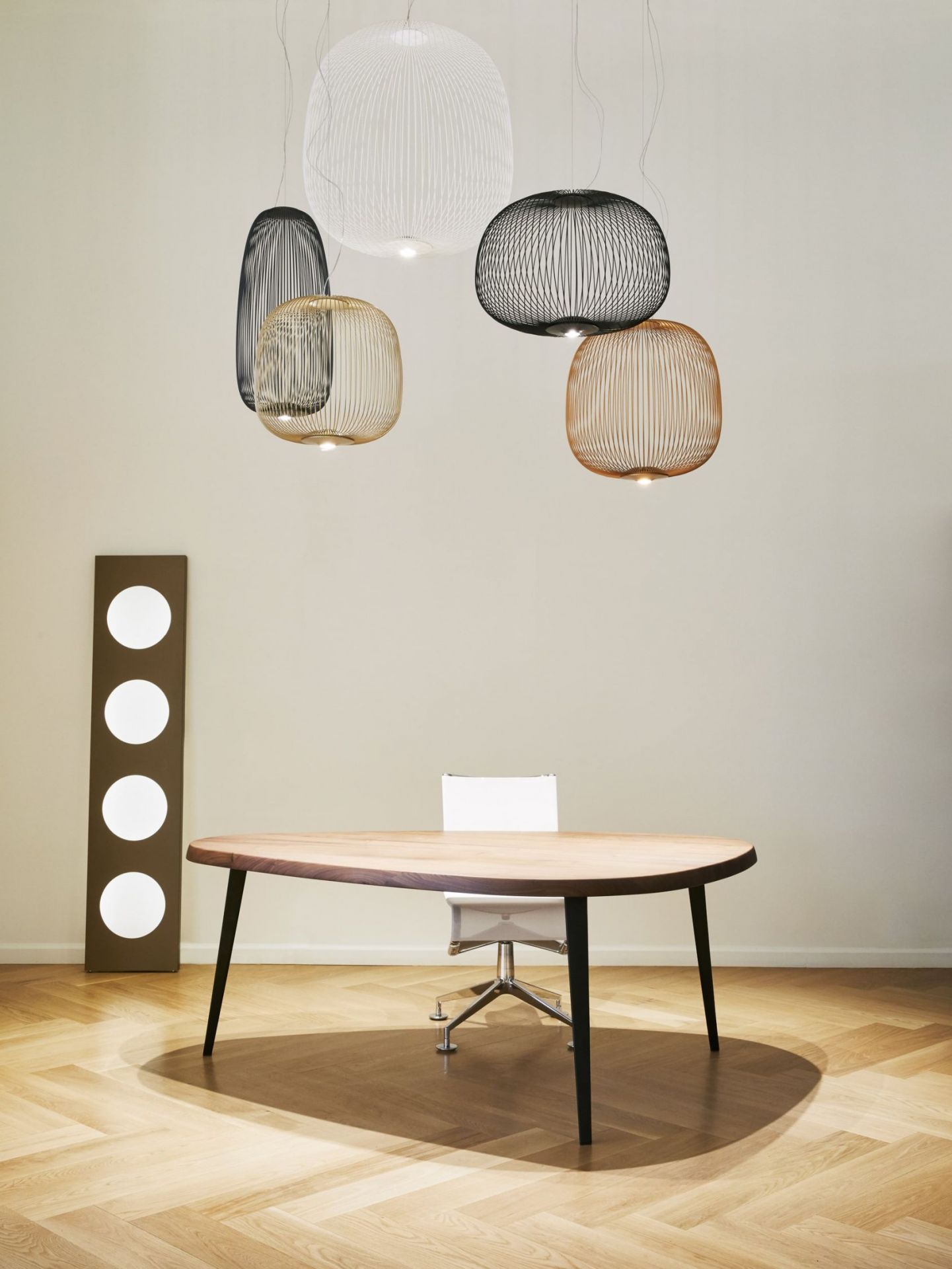 Mehrere Spokes Pendelleuchten von Foscarini, darunter eine schwarze, hängen über einem Holztisch.