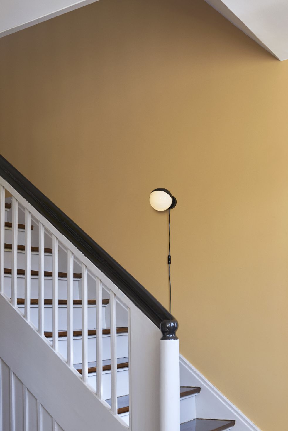 VL Studio Wandleuchte von Louis Poulsen an einer gelben Wand neben einer Treppe.