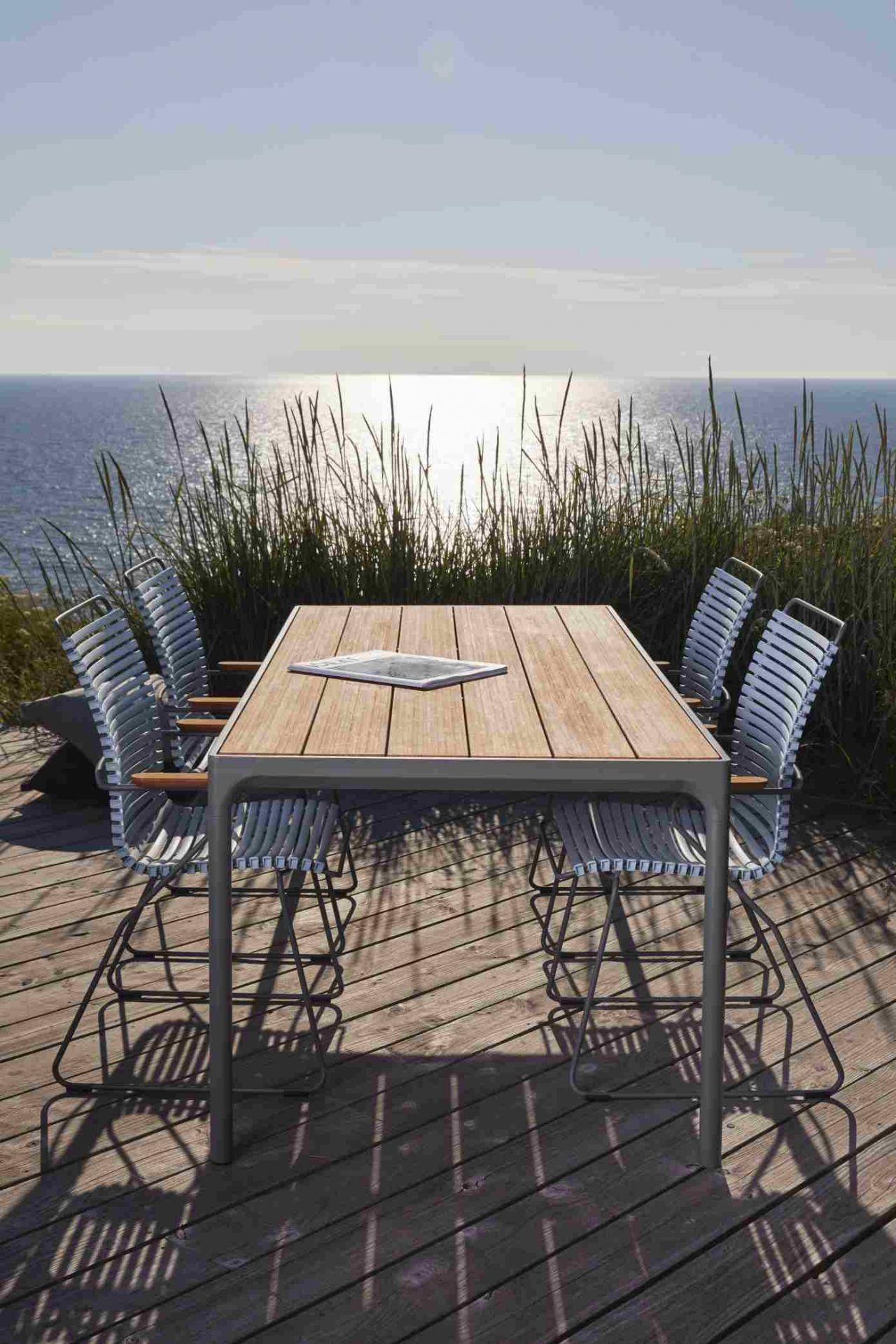 Houe Four Dining Esstisch Outdoor mit Stühlen auf Holzterrasse vor dem Meer.