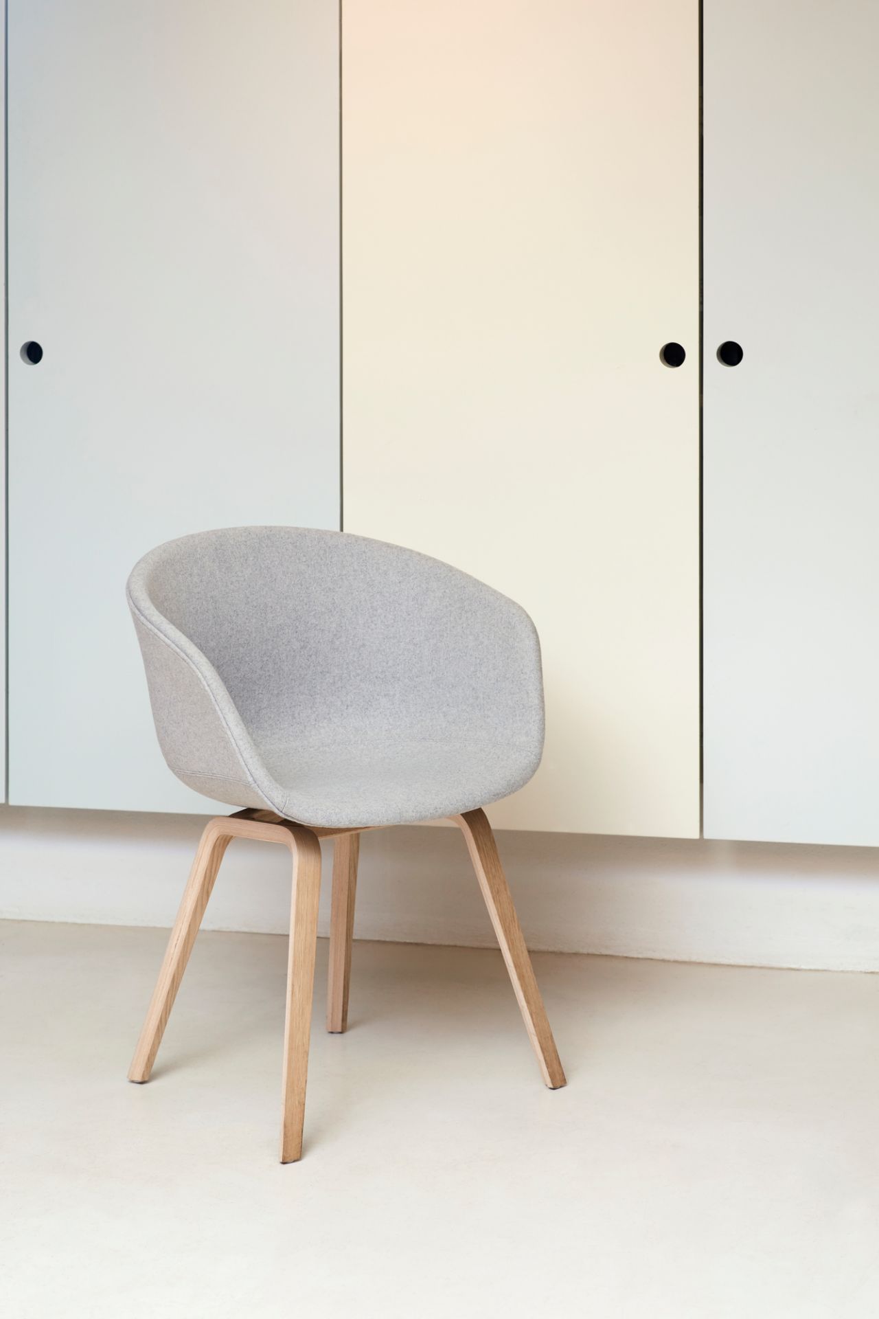 About A Chair AAC23 Stuhl von Hay, grauer Polsterstuhl mit Holzbeinen vor Schrank.