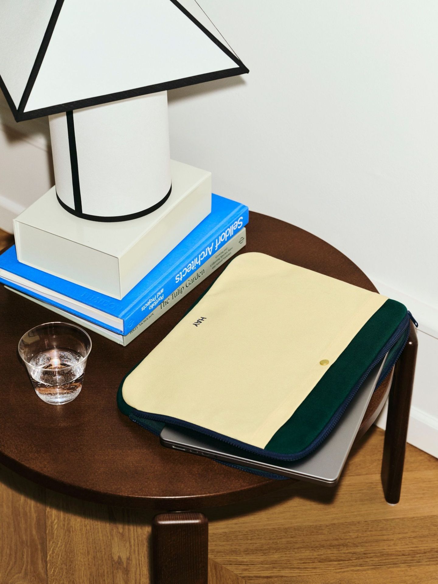 Nahaufnahme der Hay Ava Pyramid Tischleuchte auf einem Tisch mit Laptop-Tasche und Wasserglas.