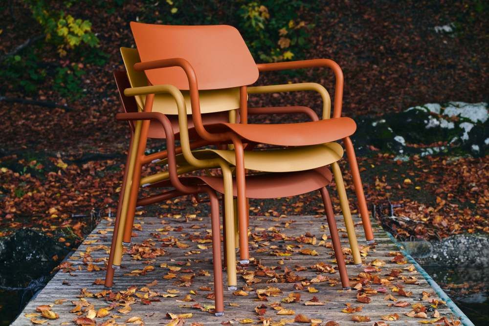 Drei Fermob Sessel, Outdoor Lounge Möbel in Herbstfarben, gestapelt auf Holzsteg mit Laub.