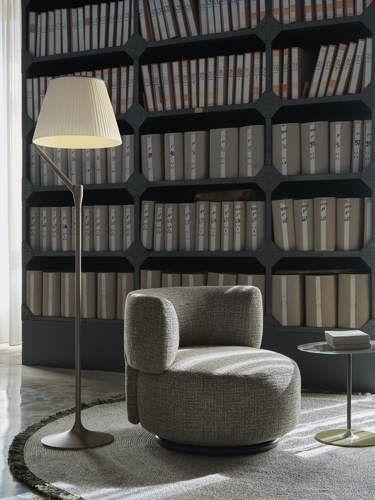 Angelo Stone Stehleuchte von Kartell neben Sessel und Beistelltisch vor Bücherwand.
