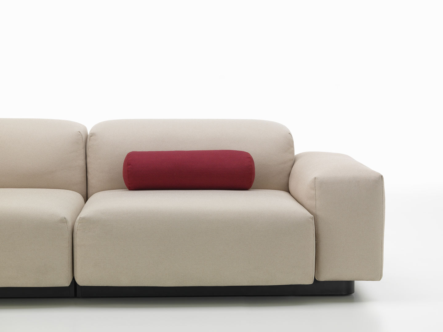 Beiges Sofa mit rotem, zylinderförmigem Vitra Kissen als Dekokissen auf der Rückenlehne.