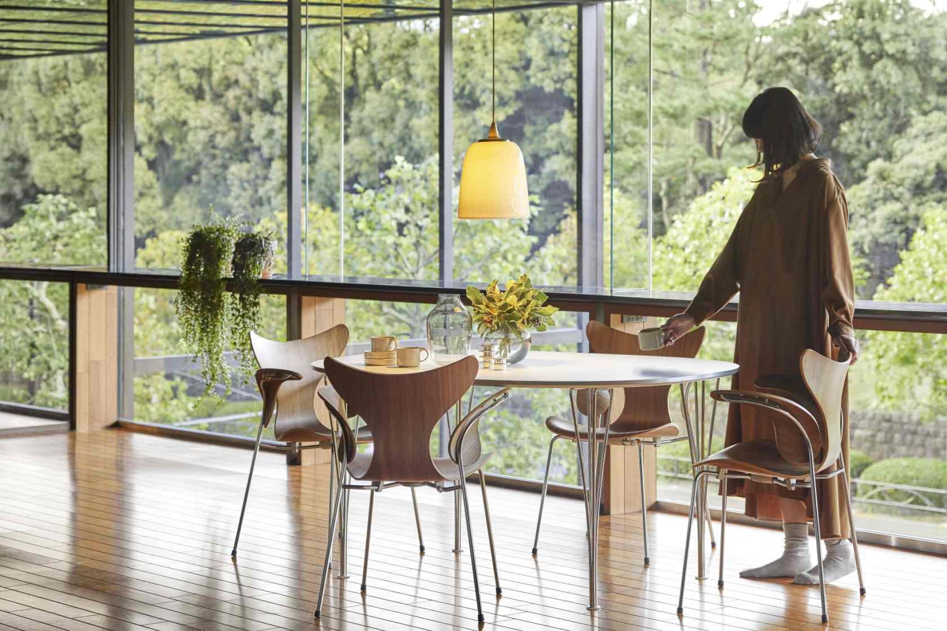 Fünf Fritz Hansen Lily Armlehnstühle aus Holz und Chrom um einen runden Esstisch in modernem Ambiente.