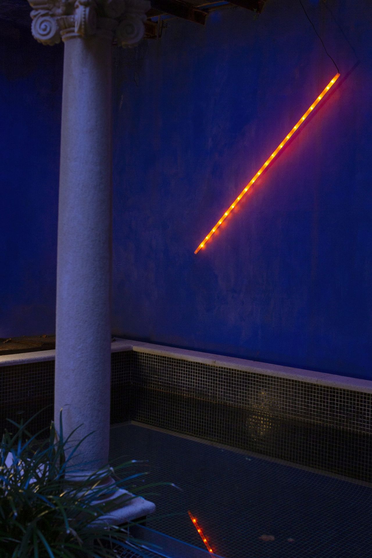 Orange LED-Leuchte an blauer Wand neben Säule, moderne Innenraumbeleuchtung für stimmungsvolles Ambiente.