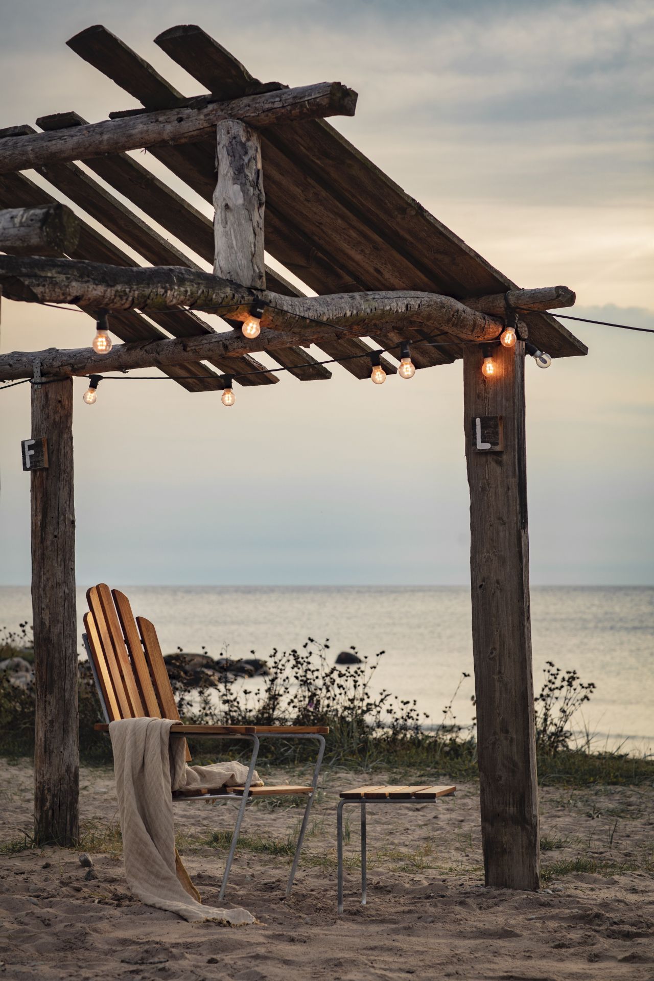 Liegestuhl A3 Eiche von Grythyttan Stalmöbler am Strand mit Meerblick und Lichterkette.