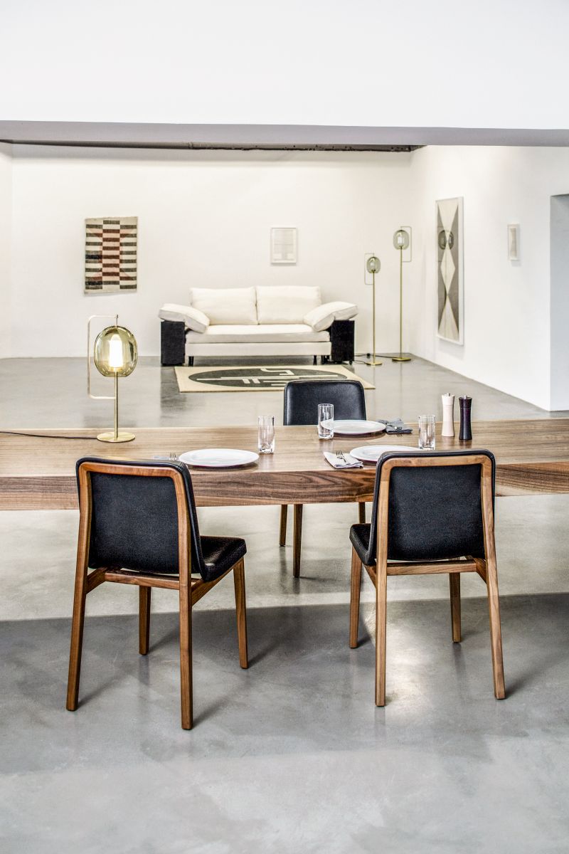 Esszimmer-Szene mit ClassiCon St. Tropez Teppich (300x250cm) unter weißem Sofa, Holztisch mit Gedeck und Stühlen.