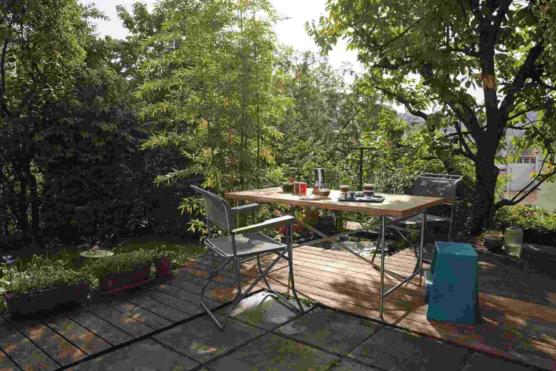 Eiermann Tisch mit Stahlgestell und zwei Stühlen auf einer Terrasse mit üppigem Grün.