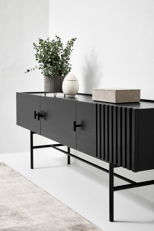 Schwarzes Sideboard von Woud mit Holzstruktur, minimalistischen Griffen und dekorativen Elementen im modernen Wohnzimmer.