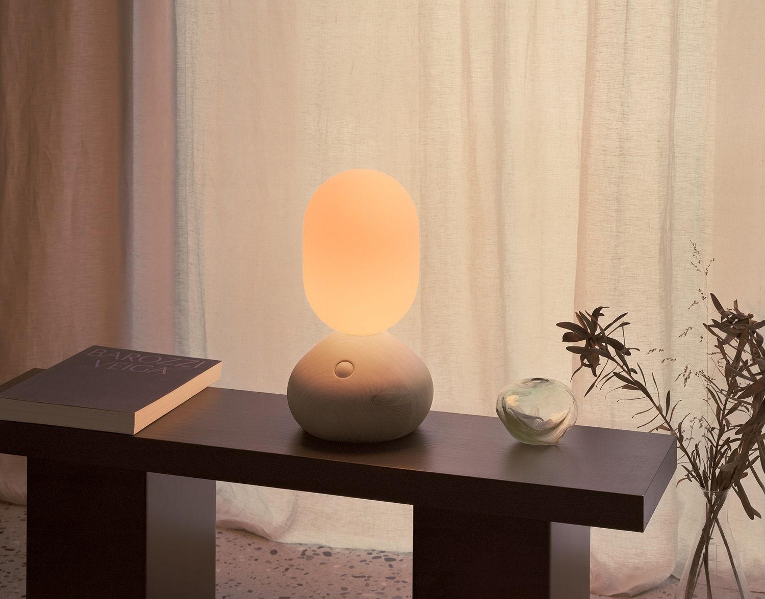 Sun Home Lichtskulptur Tischleuchte in Grau auf dunklem Tisch mit Buch und Dekoration.