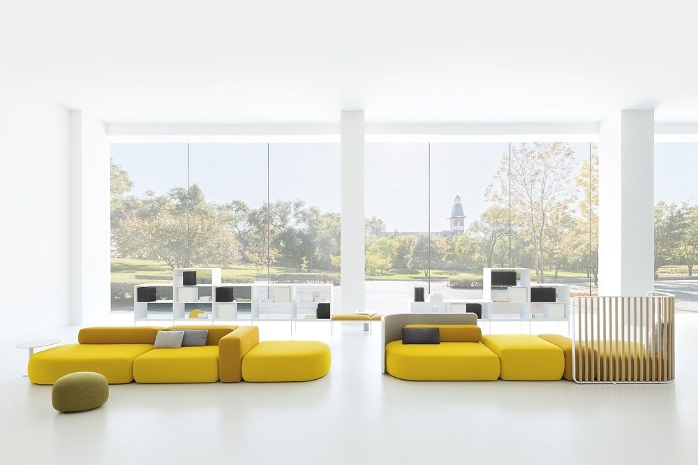 Gelber PLUS D215 Pouf und Einsitzer La Palma in modernem, hellem Raum mit großem Fenster.