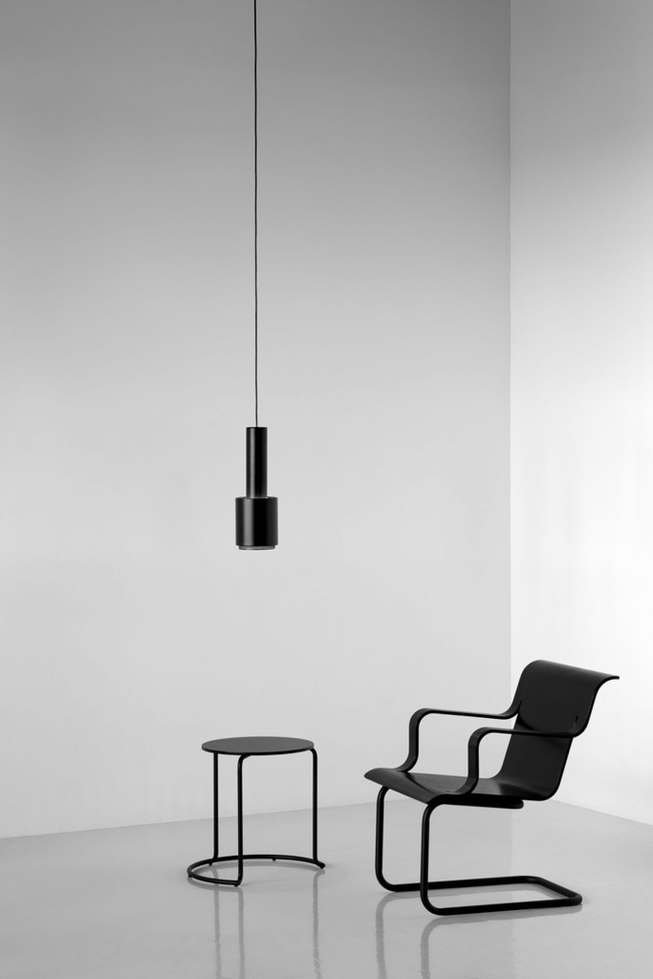 Schwarzer Artek 606 Beistelltisch aus Holz neben einem Stuhl und einer Hängelampe in minimalistischem Raum.