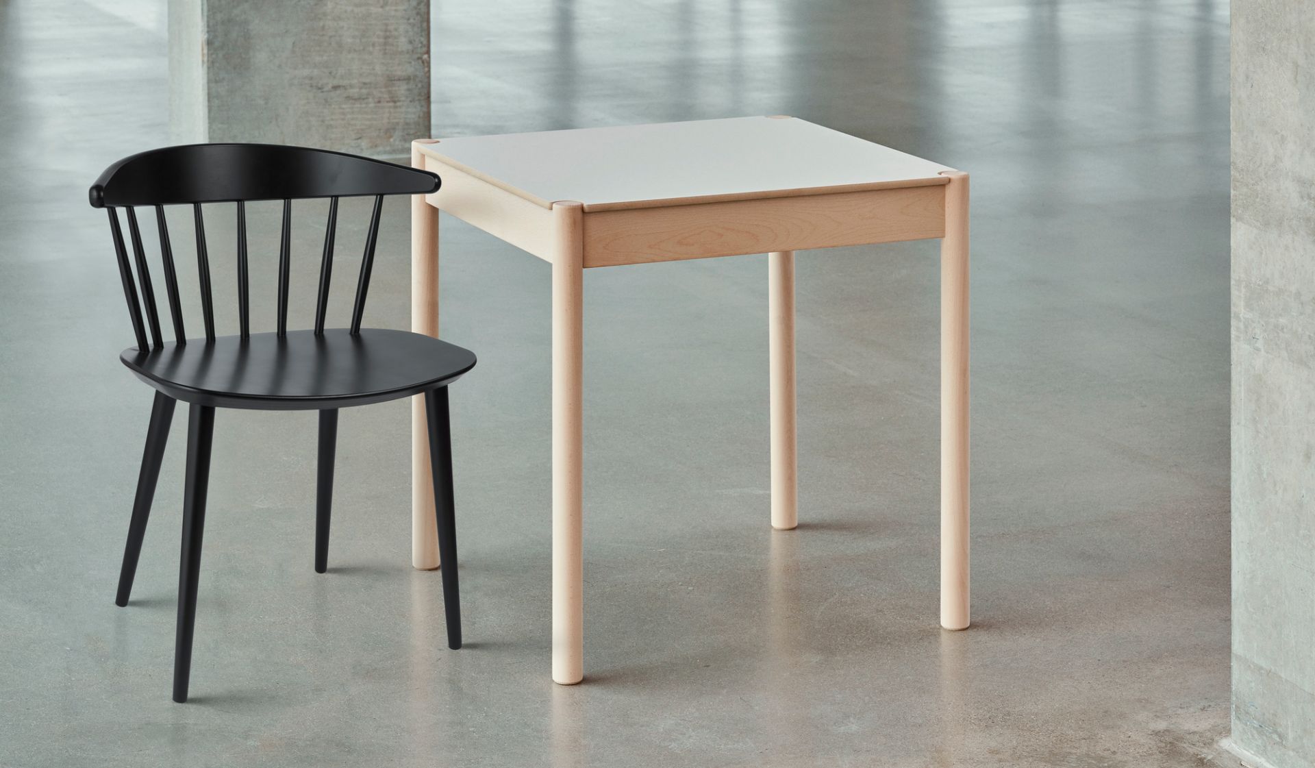 Schwarzer J104 Chair Stuhl von Hay neben einem hellen Holztisch auf grauem Untergrund.