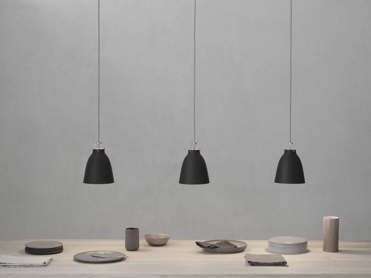 Drei schwarze Caravaggio Pendelleuchten von Fritz Hansen hängen über einem gedeckten Esstisch in minimalistischem Design.