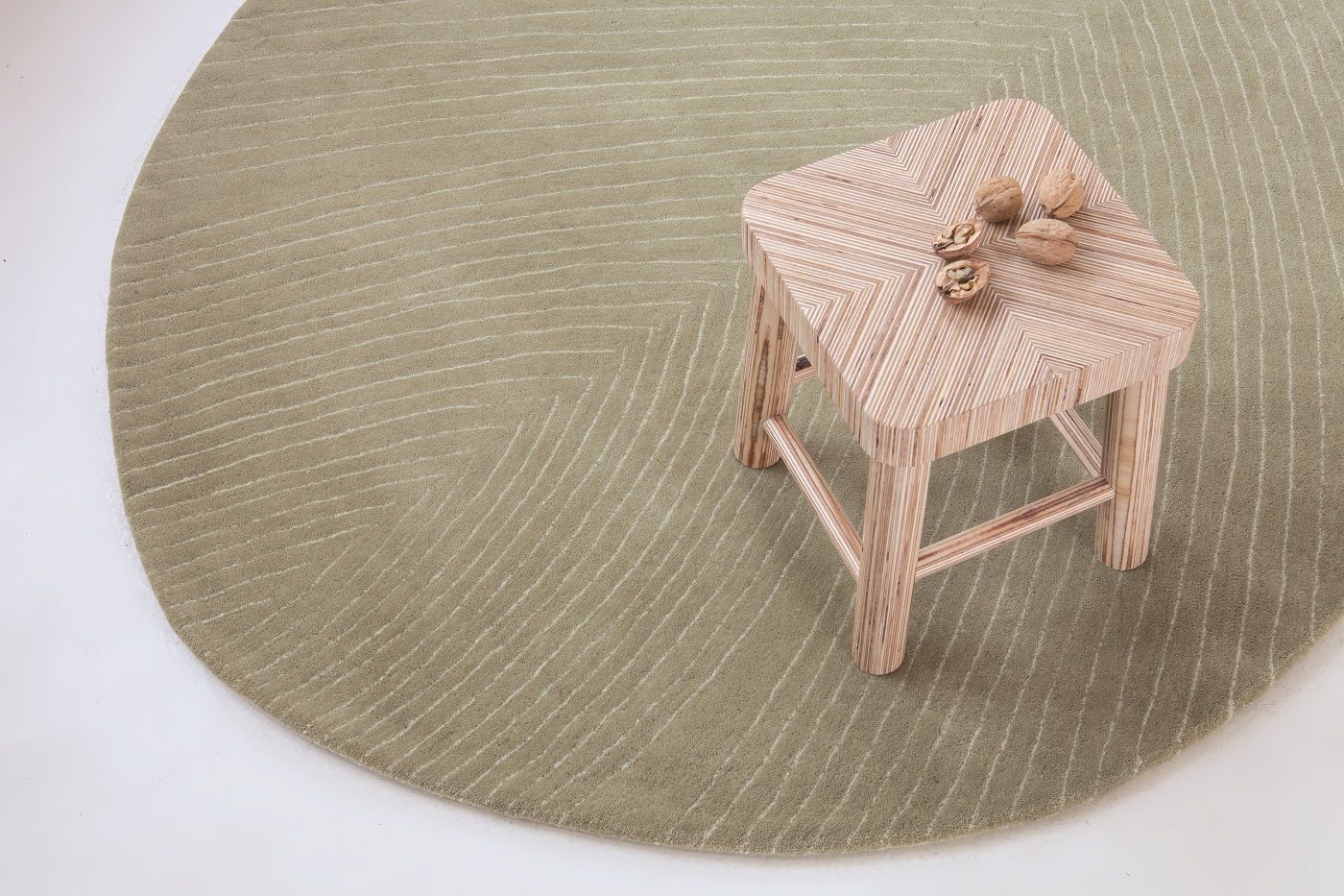 Runder, olivgrüner Teppich mit Muster und Holzschemel, Nanimarquina Teppich, modernes Wohnaccessoire.